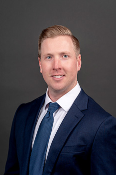 Headshot of Jon Barry, who smiles while wearing a dark blue suit and a dark blue tie