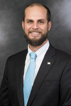 Headshot of Josh Paton, who smiles while wearing a black suit and a light blue tie