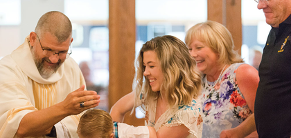 Faith holds Noah as he is baptized by Father David Veit