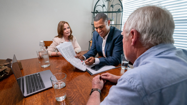 Senior couple sitting at a table with an agent, discussing work together.