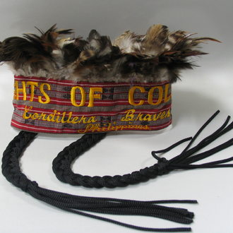 Contemporary headdress crowned with feathers and two hanging braids. Headband embroidered with text “Knights of Columbus Cordillera Braves Phillippines.”
