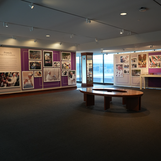 Color photo of a museum gallery with photographs and items related to Pope Francis’ international trips on exhibit.