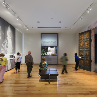 Fotografía de la galería del museo con la réplica de las Puertas Sagradas, imágenes del Papa Juan Pablo II en las paredes y visitantes recorriendo la sala.