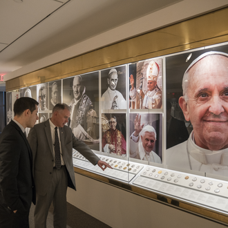 Photo of the Papal Gallery with two men in suits looking at a case of papal medals.