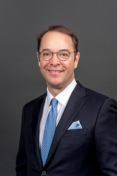 Headshot of Peter Anderson, who smiles while wearing a black suit and a blue tie