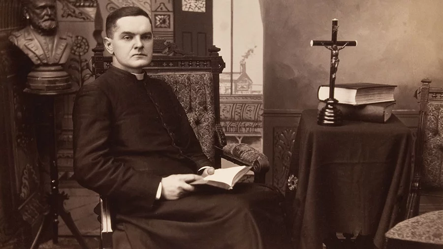 Father Michael J. McGivney seated in a rectory setting circa 1880