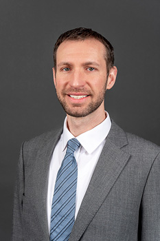 Headshot of Ted Mulrane, who smiles while wearing a light grey suit and a blue tie