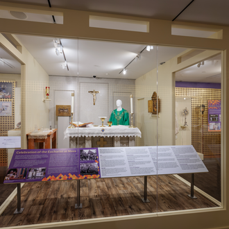 Photo of the temporary exhibit "True Presence: The Eucharist in History and Art." Depicts case with setup of altar during  Mass.