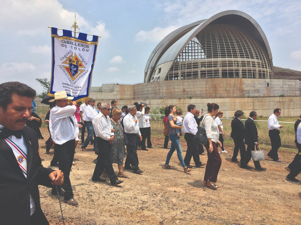 Knights marching holding a "Caballeros de Colon" banner, with a building in the background.