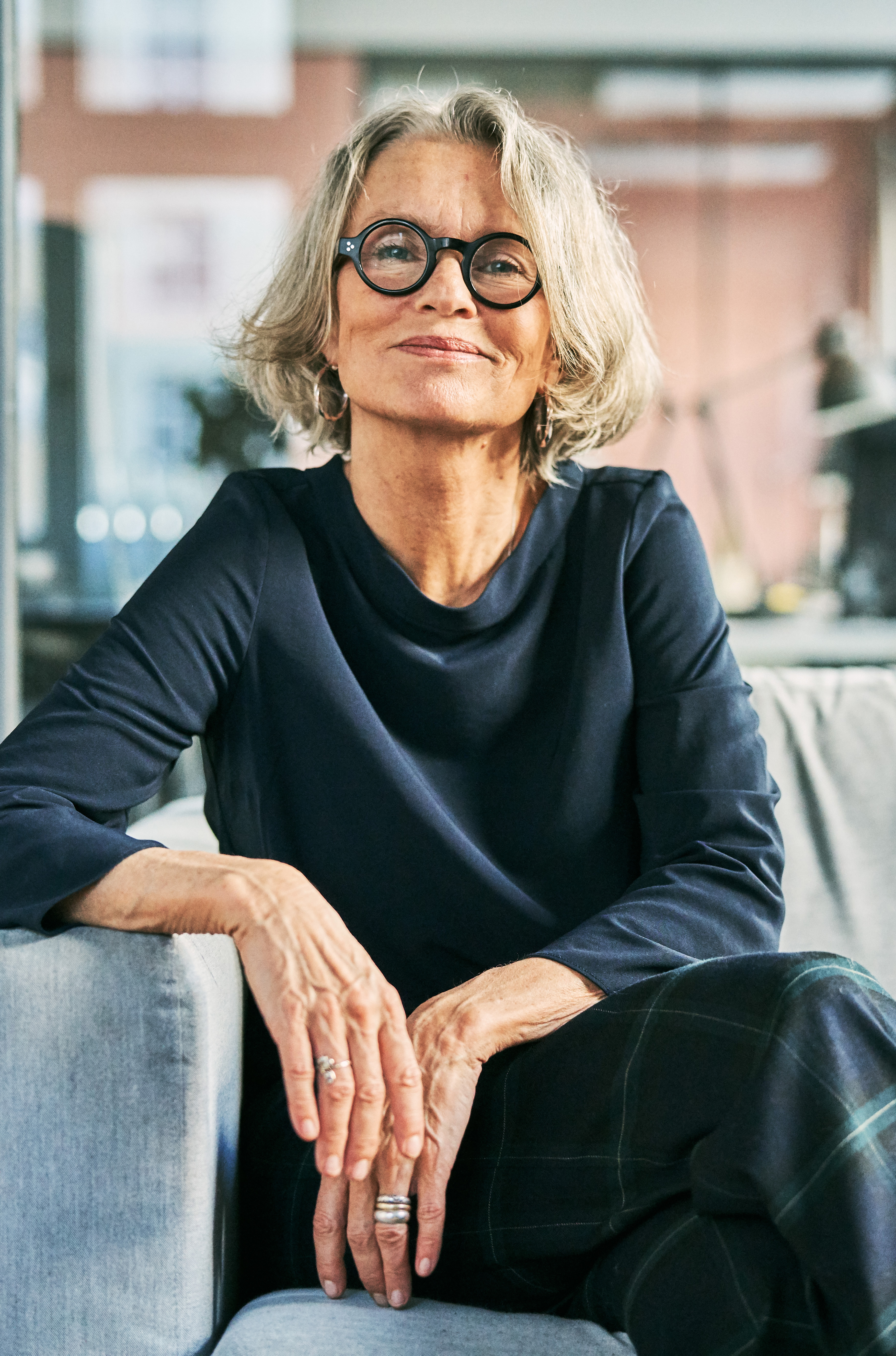 A woman sitting and smiling with gray hair and round glasses.